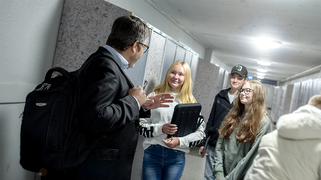 Daniel Ekwall pratar med tre högstadielever i en skolkorridor. 