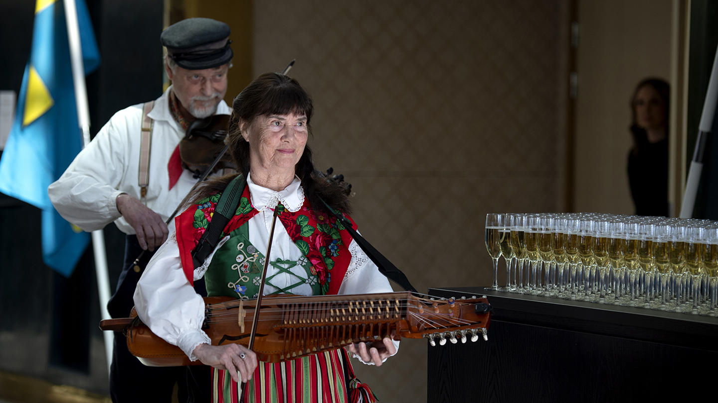 Spelemännen på väg ut från kongressen, förbi ett bord med fyllda champagneglas.