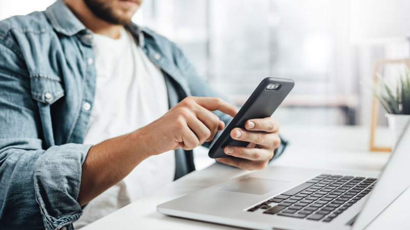 Person with mobile sitting by a laptop