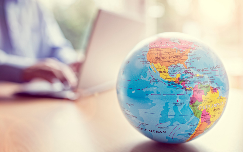 Globe in front of person typing on a laptop